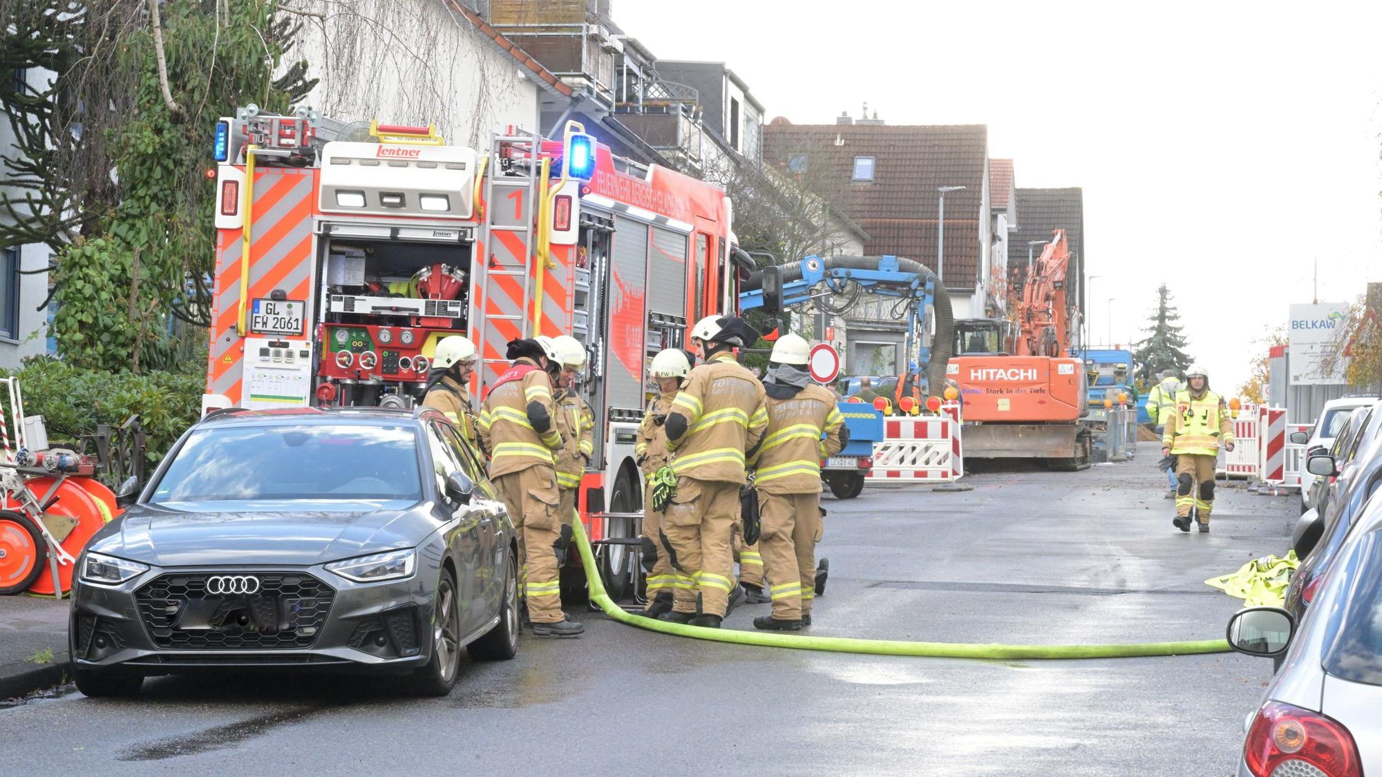 Feuerwehrleute stehen auf einer Straße, im Hintergrund ist ein Bagger zu sehen.