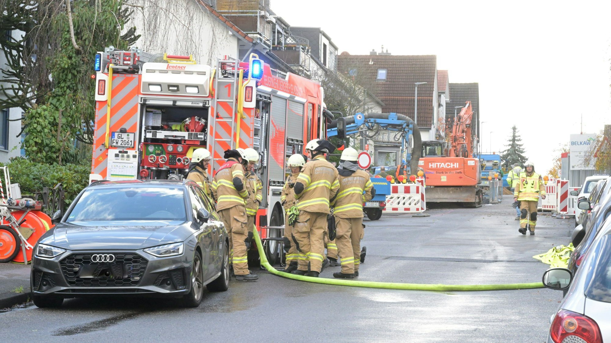 Feuerwehrleute stehen auf einer Straße, im Hintergrund ist ein Bagger zu sehen.