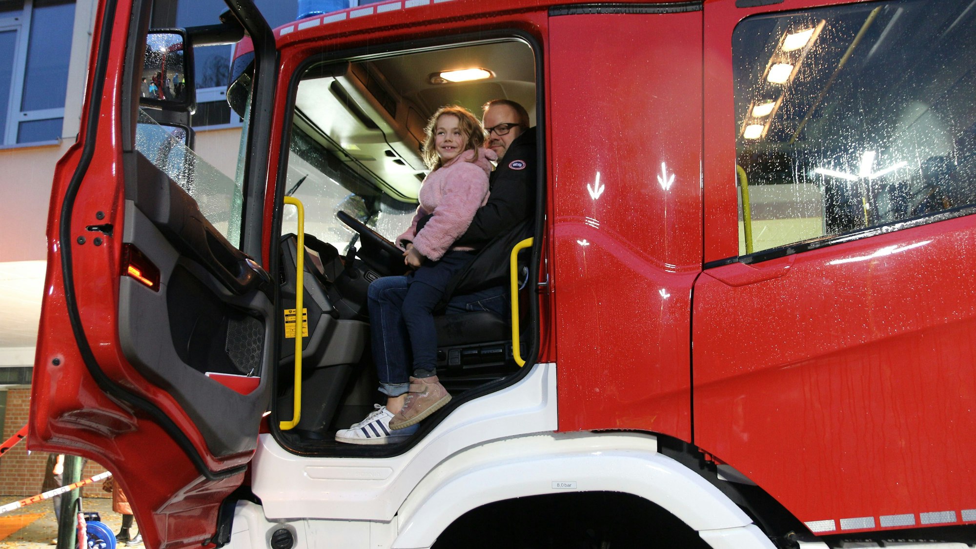 Ein Vater und seine Tochter, die auf seinem Schoß sitzt, schauen aus einem Lkw auf die Straße.