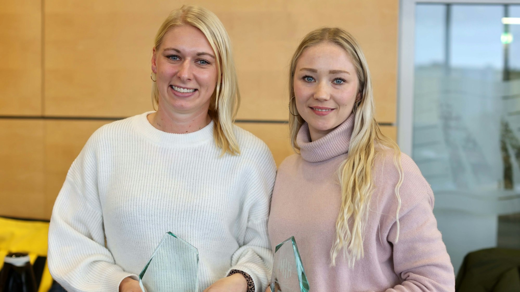 Zwei Frauen halten eine Auszeichnung in der Hand und grinsen in die Kamera.