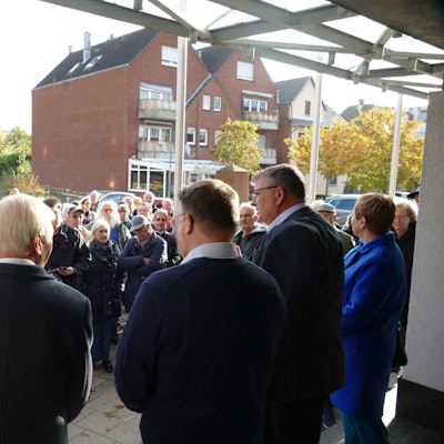 Männer und Frauen stehen vor einem Verwaltungsgebäude.