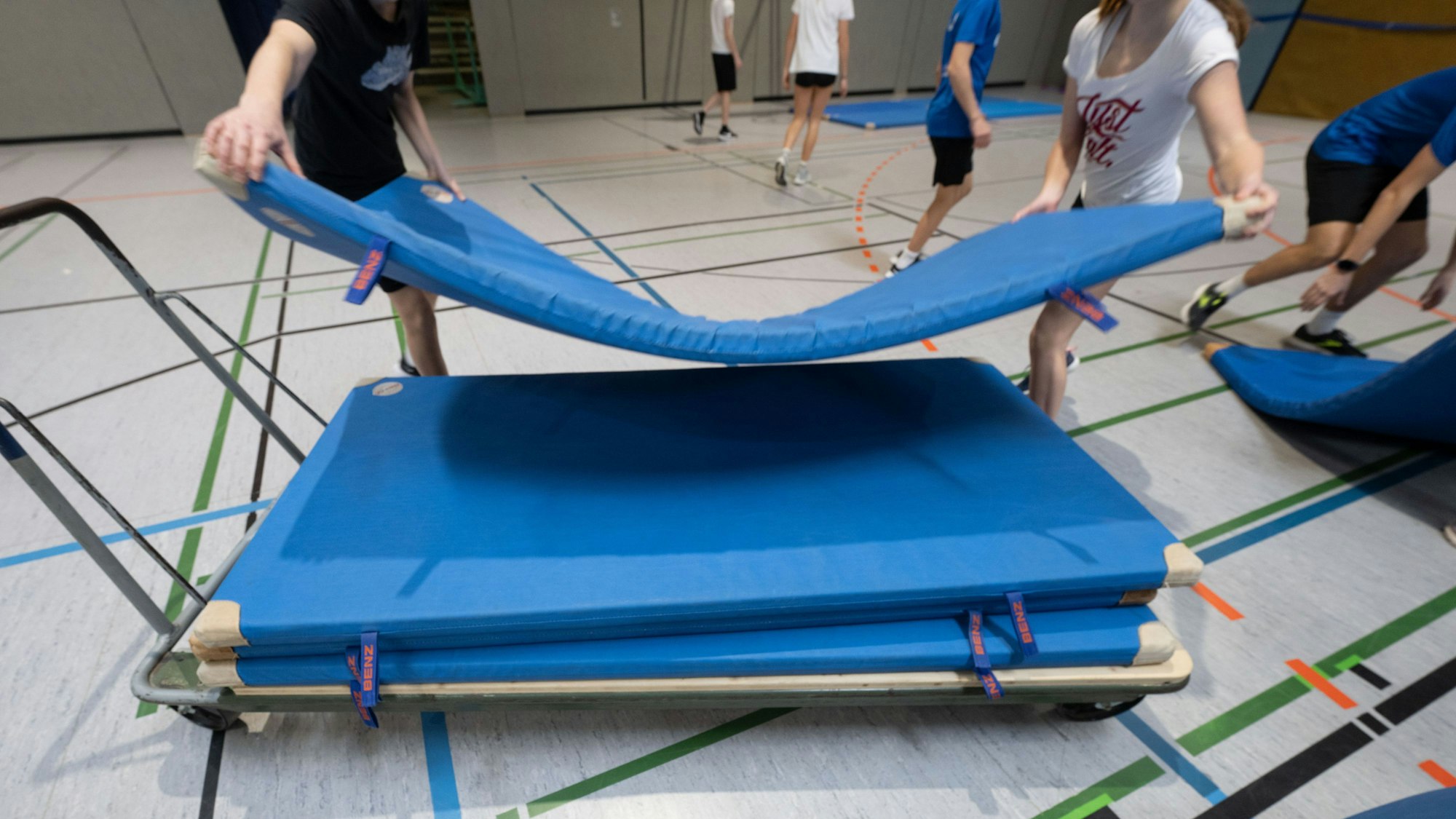 Schüler und Schülerinnen stapeln blaue Turnmatten.