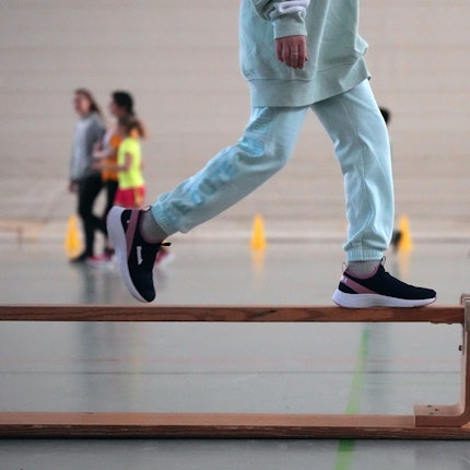 Eine Schülerin läuft im Sportunterricht über eine umgedrehte Holzbank.