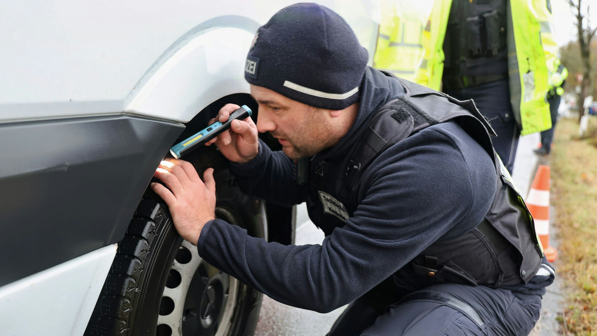 Ein Polizeibeamter leuchtet mit einer Taschenlampe zwischen Rad und Kotflügel hindurch unters Fahrzeug.