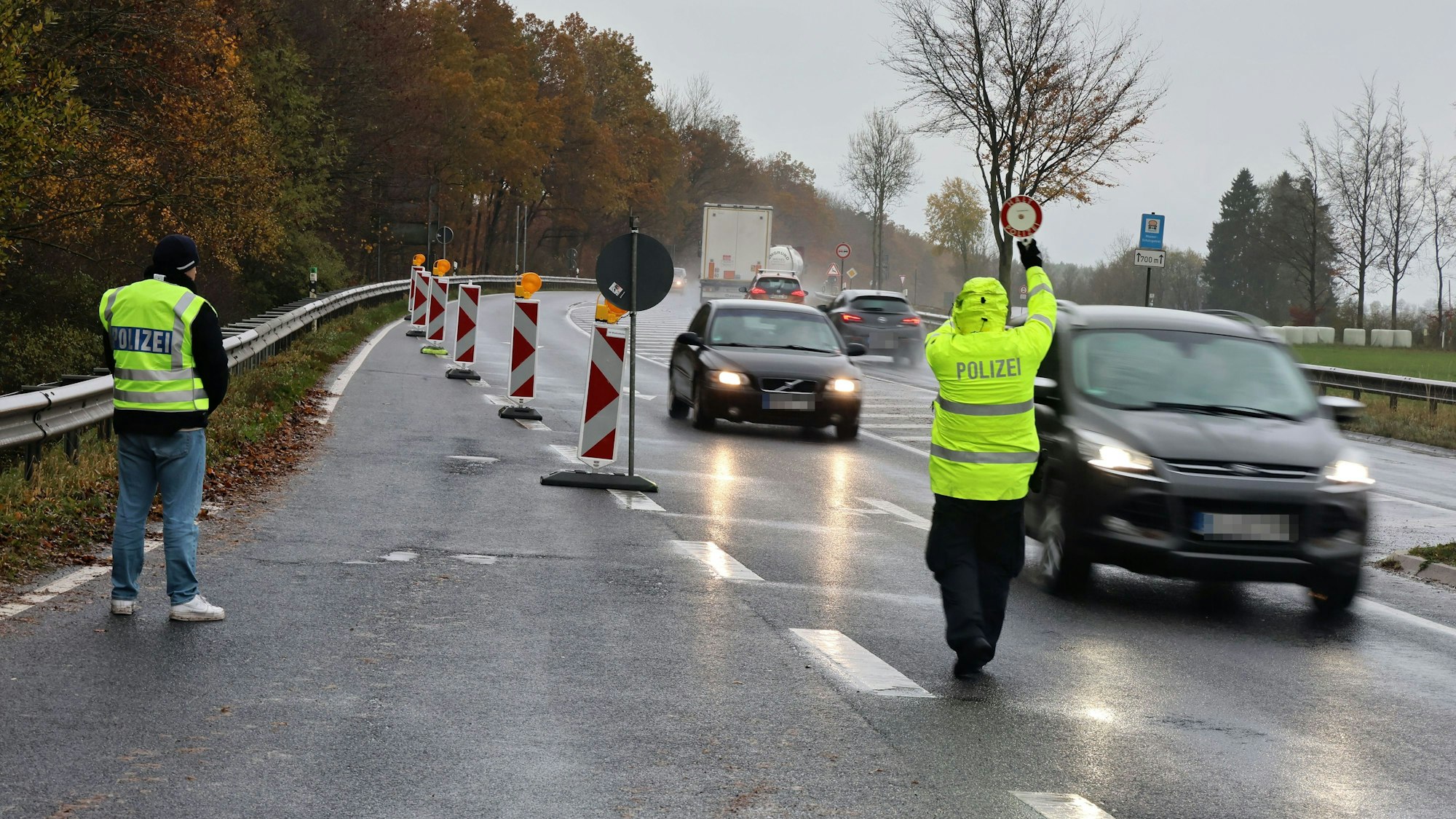 Zwei Polizeibeamte winken im strömenden Regen Fahrzeuge aus dem fließendem Verkehr.