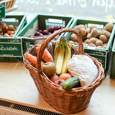 Ein zugeschnürtes Stoffsäckchen mit Nudeln liegt neben Obst und Gemüse in einem Korb in einem "Unverpackt"-Laden.