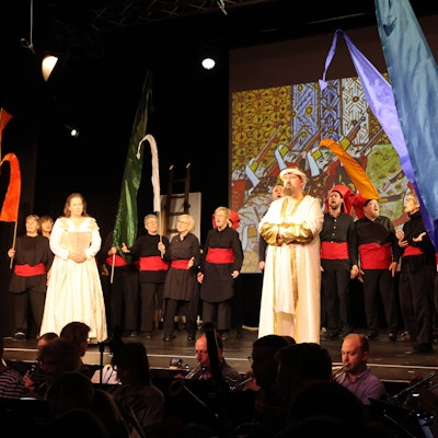 Auf einer Bühne stehen Sänger vor einem Chor.