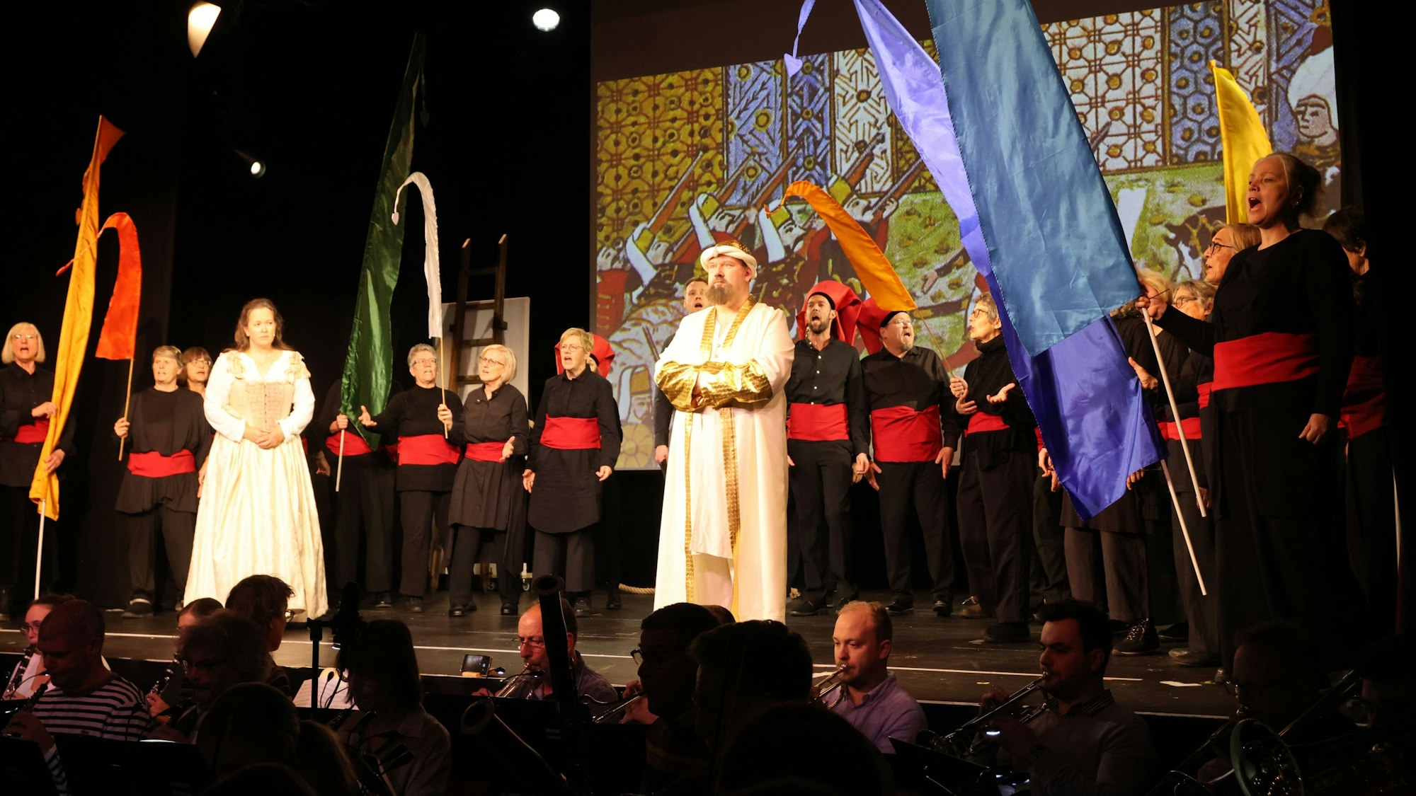 Auf einer Bühne stehen Sänger vor einem Chor.