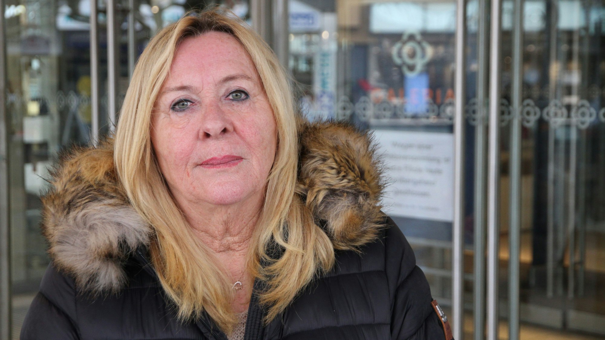 Eine Frau in einem Wintermantel steht vor dem Eingang eines Kaufhauses.
