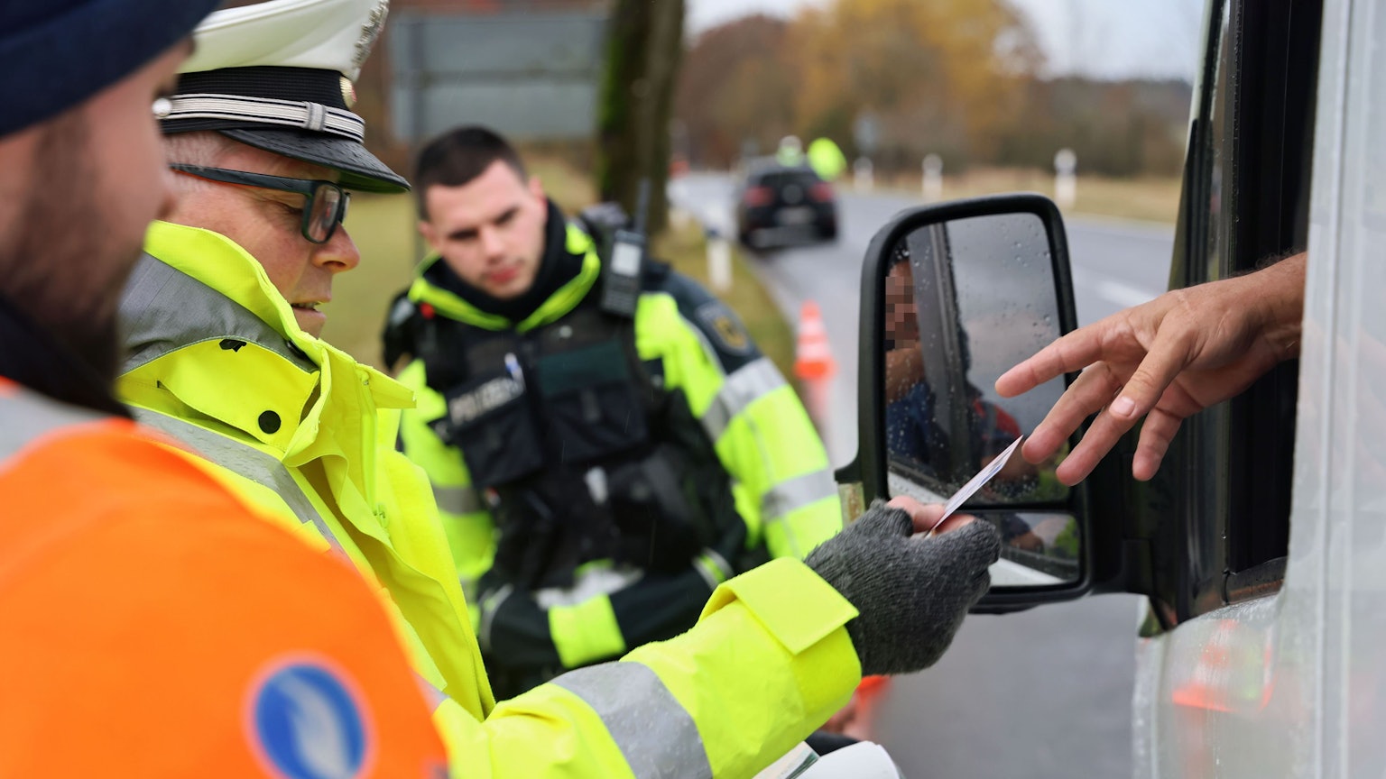 Polizisten kontrollieren am Straßenrand einen PKW durch dessen Fenster hindurch.