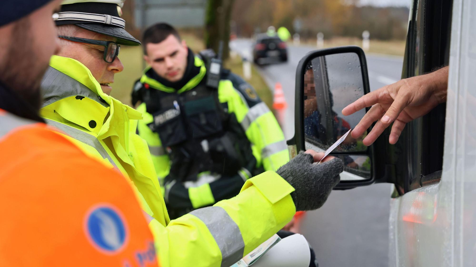 Ein Fahrer reicht seine Papiere aus dem Fenster. Jeweils ein Polizist aus Deutschland, den Niederlanden und Belgien stehen bereit.