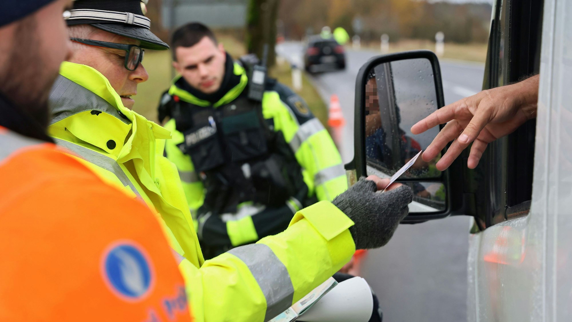 Polizisten kontrollieren am Straßenrand einen PKW durch dessen Fenster hindurch.