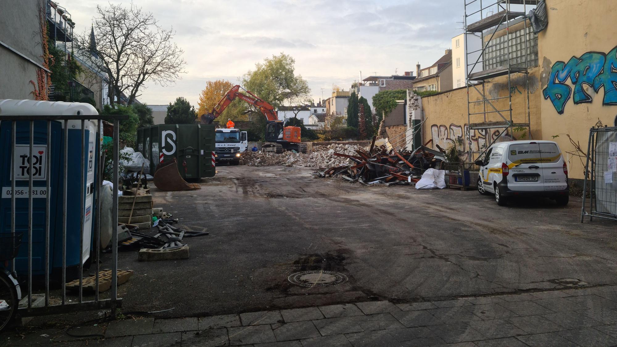 Blick auf ein großes Grundstück, auf dem Trümmer per Bagger auf einen Lastwagen geschaufelt werden.