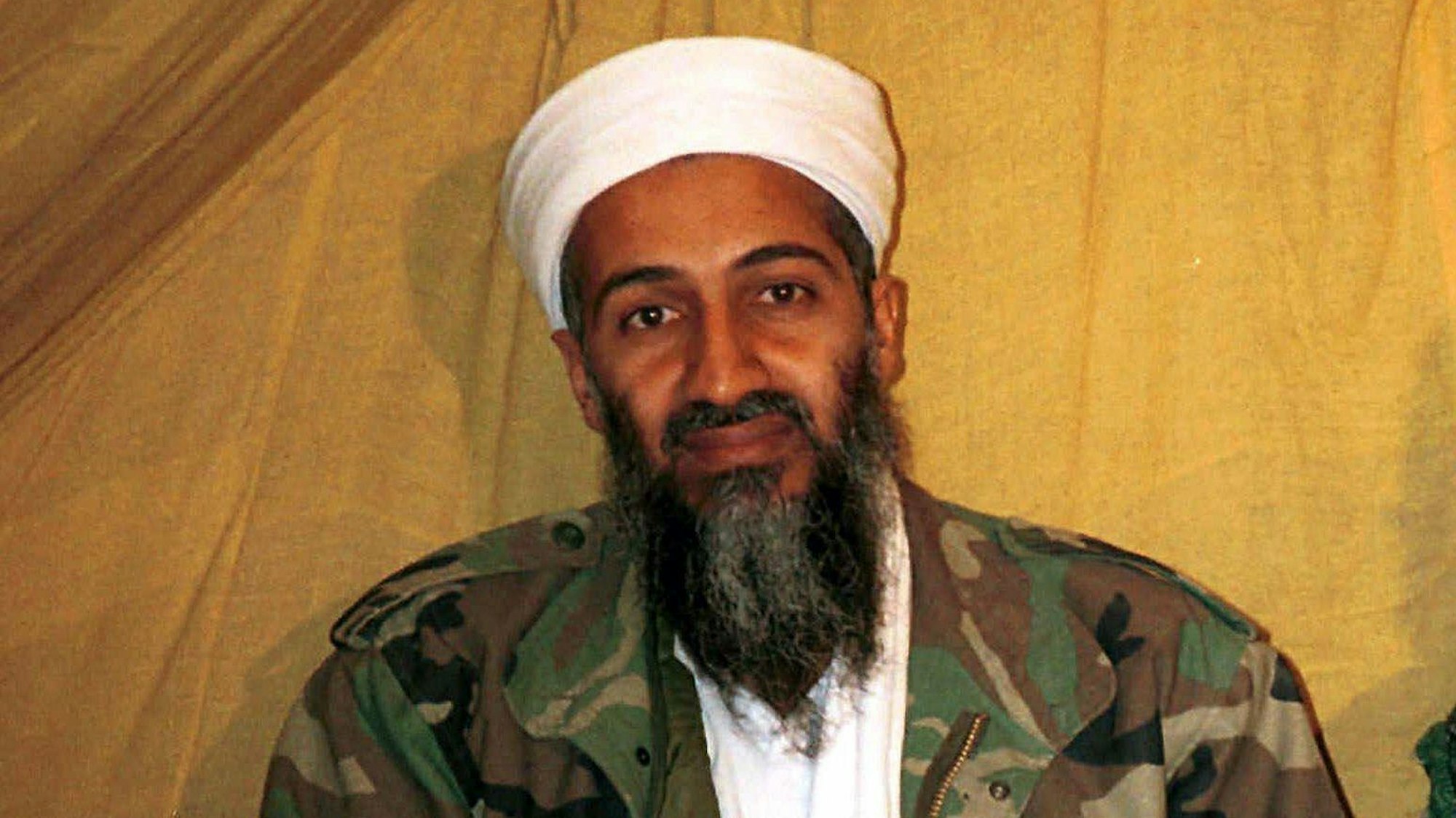 Osama bin Laden in Camouflage-Jacke vor einem hellen Hintergrund