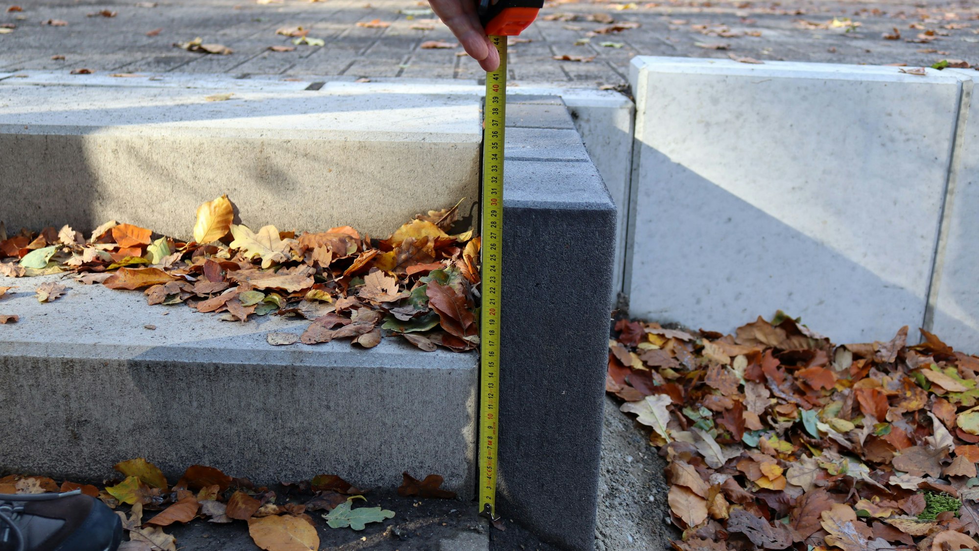 Ein Maßband wird an einen Randstein gehalten. Zu erkennen ist, dass es von der Treppe des Vorgartens zur Straße 30 Zentimeter hoch ist.