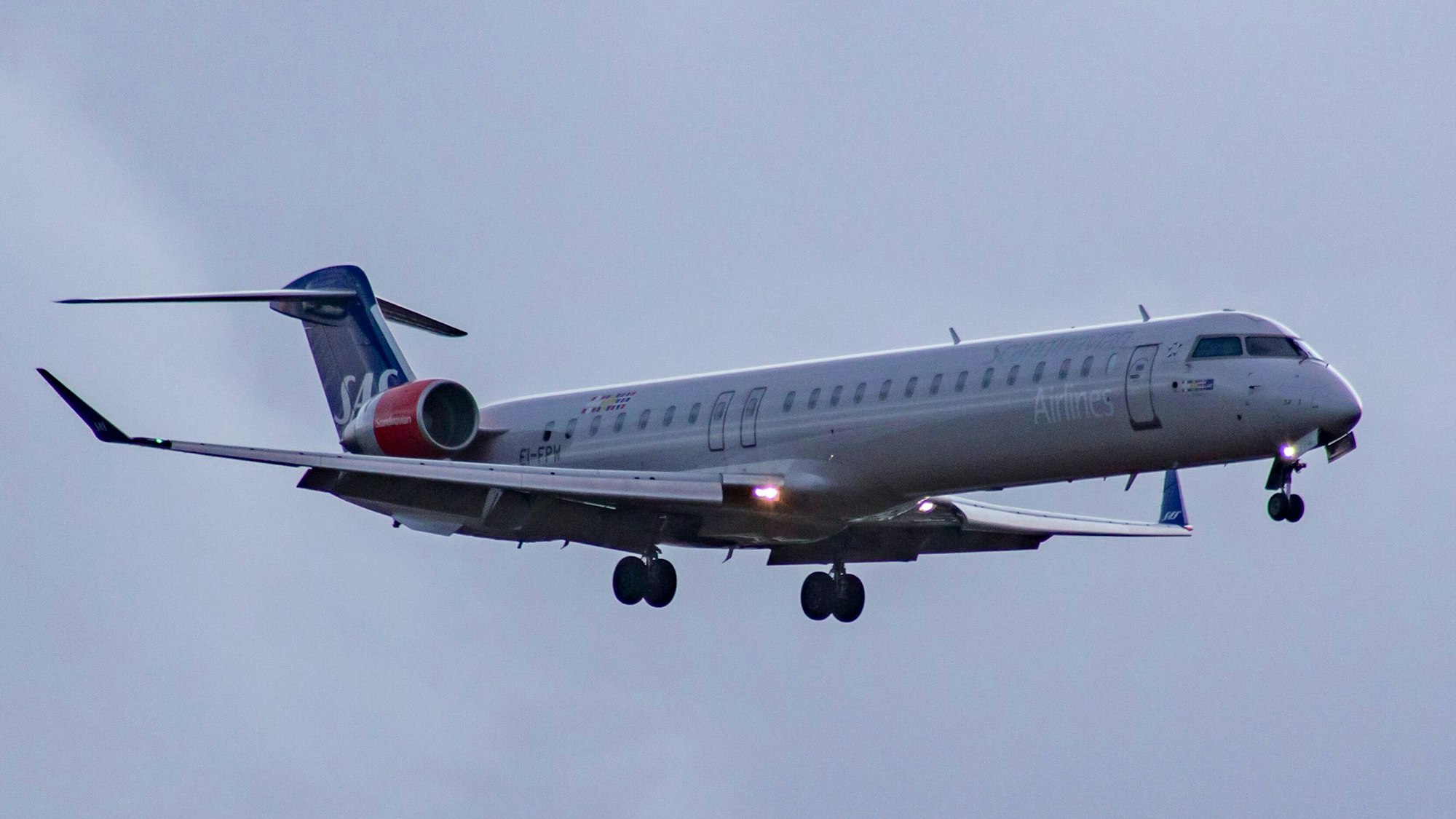 Ein Flugzeug vom Typ Bombardier CRJ-900 der skandinavischen Fluggesellschaft SAS Airlines bei schlechtem Wetter im Landeanflug auf einen Flughafen. An der Maschine sind mehrere Warnleuchten zu sehen. (Symbolbild)