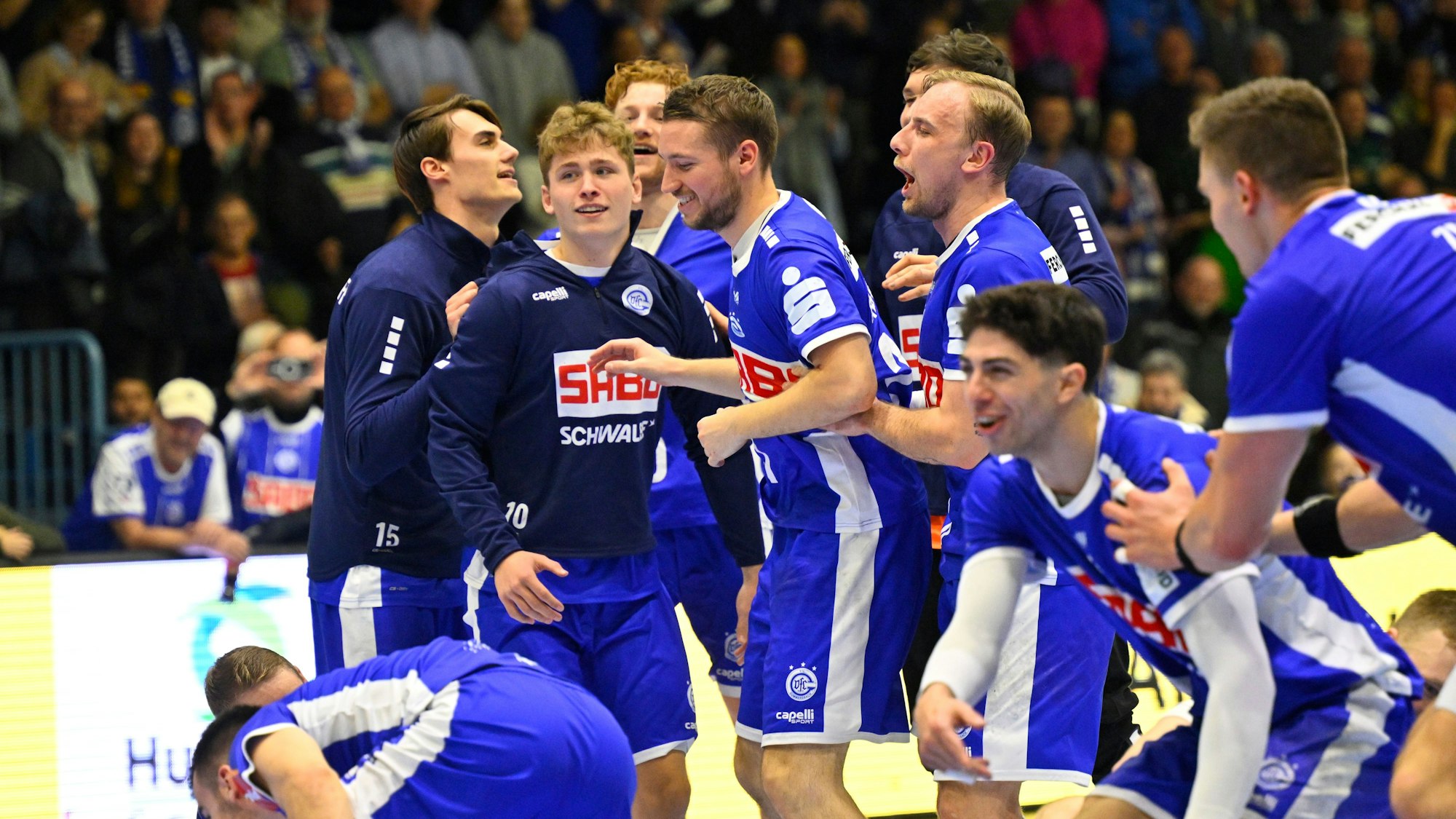 Mehrere Spieler des VfL Gummersbach stehen als Gruppe zusammen und freuen sich über den Sieg. In ihrer Mitte ist auch Spieler Finn Schroven.