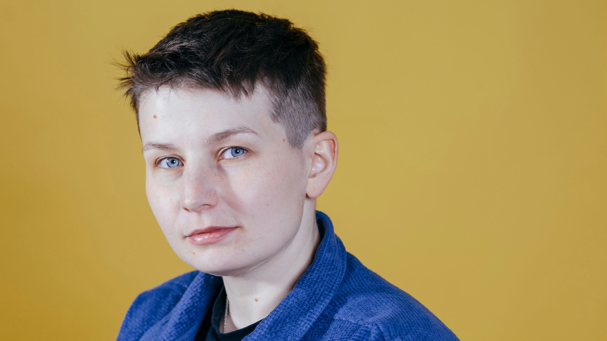 Sara Gryzbek in blauer Jacke vor gelbem Hintergrund.