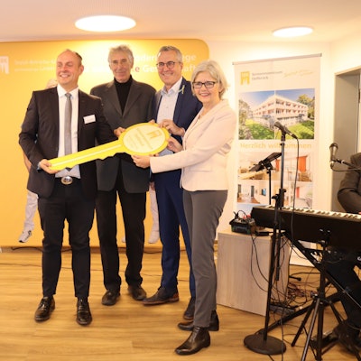 Drei Männer und eine Frau halten gemeinsam einen überdimensionalen Schlüssel.