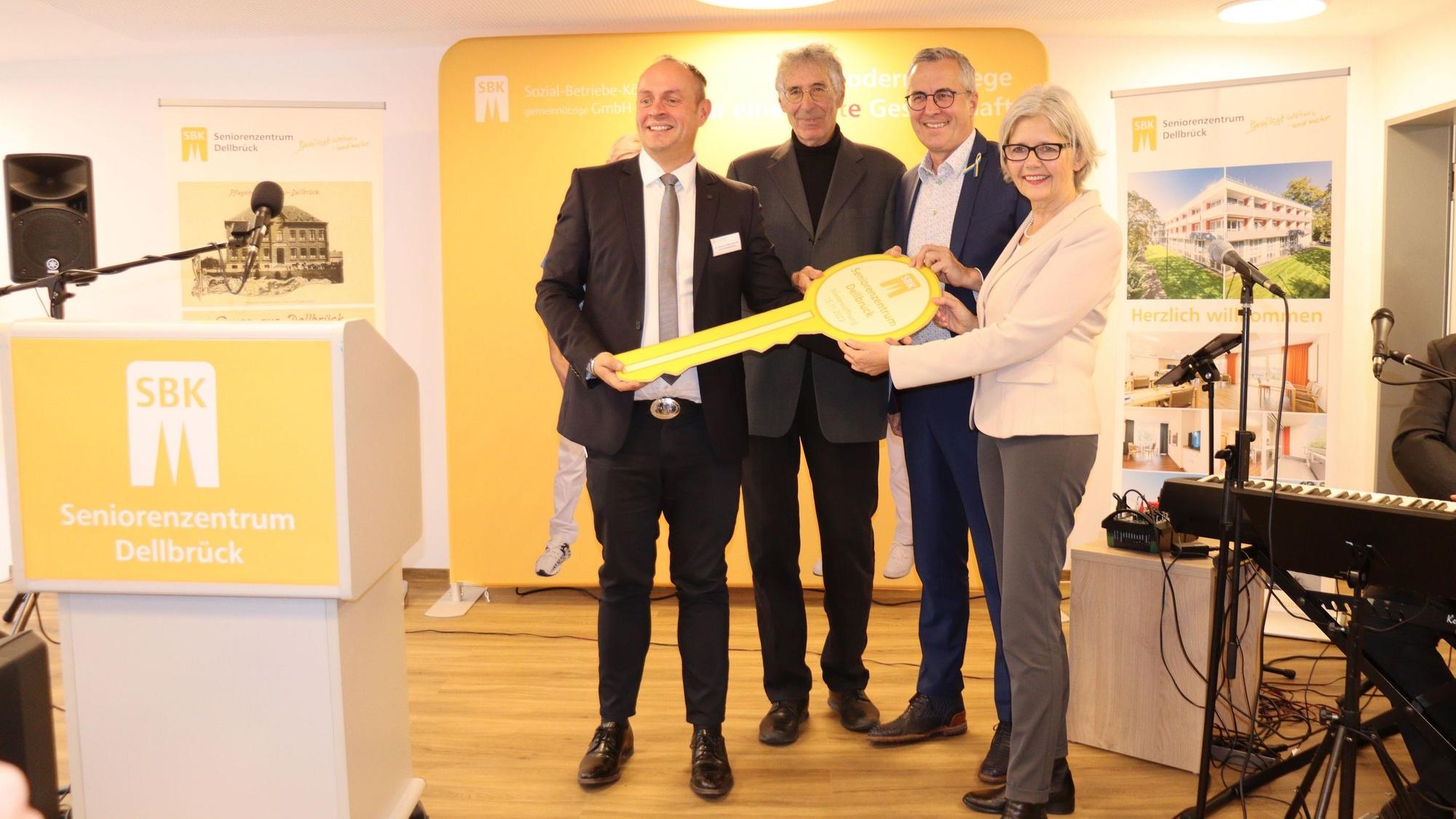 Drei Männer und eine Frau halten gemeinsam einen überdimensionalen Schlüssel.