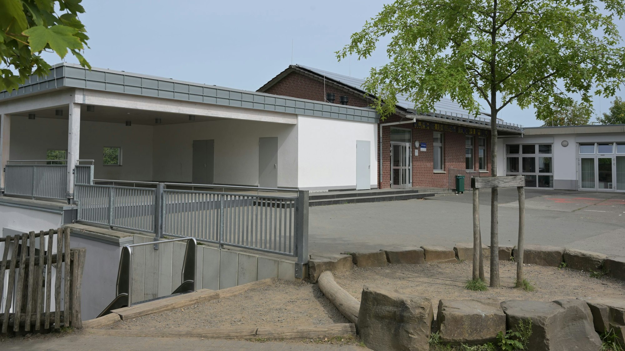 Der L-förmige Bau der KGS Burg Berge in Blecher formiert sich um den Pausenhof. Im Vordergrund ein Spielgelände mit einem jungen Laubbaum.