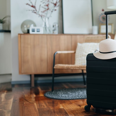 In einem Wohnzimmer steht ein kleiner schwarzer Koffer, darauf liegt ein weißer Hut