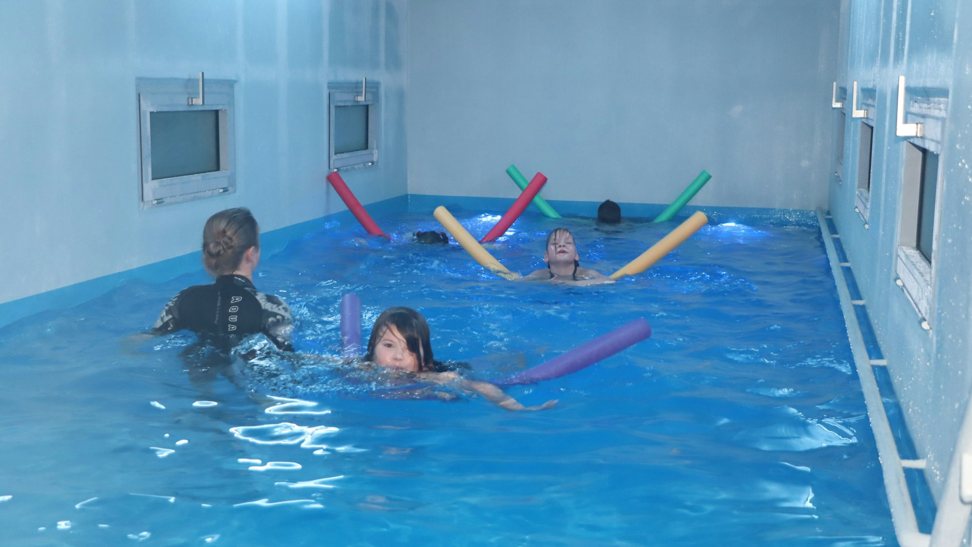 Kinder schwimmen mithilfe von Poolnudeln in einem mobilen Schwimmcontainer.