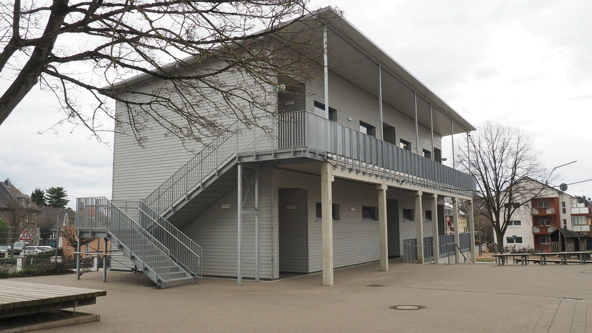 Das Foto zeigt ein graues zweigeschossiges Gebäude mit Außentreppe.