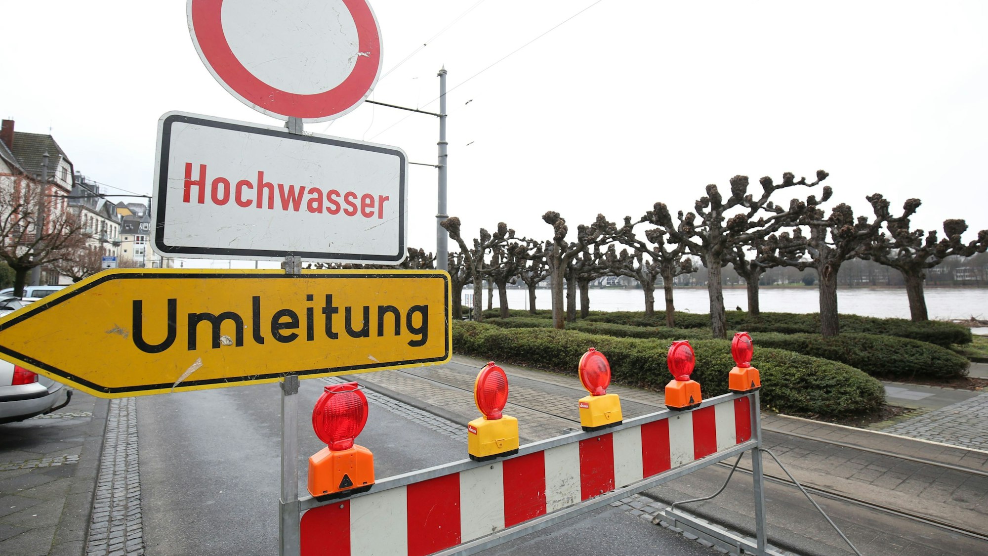 Ein rot-weiße Speerbake steht auf der Rheinallee, auf einem Schild steht „Hochwasser“ und ein Umleitungsschild weist den Weg.