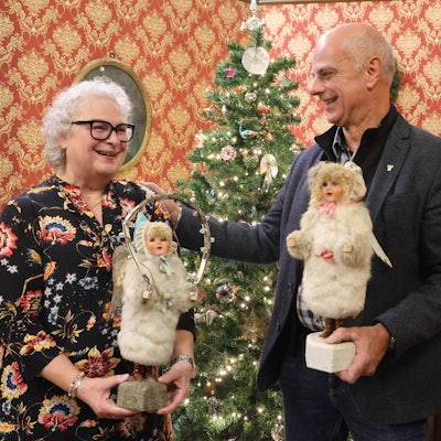 Eine Frau und ein Mann halten Engel-Figuren vor einem Weihnachtsbaum.