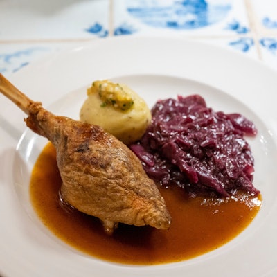 Ein gebratenes Stück Gans liegt mit Sauce, Rotkohl und Kloß auf einem Teller.