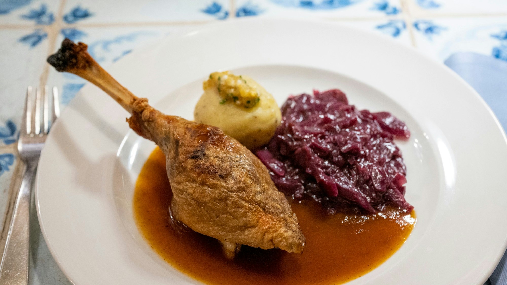 Ein gebratenes Stück Gans liegt mit Sauce, Rotkohl und Kloß auf einem Teller.