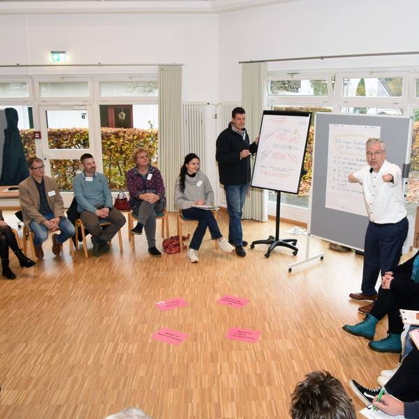 Unter der Moderation von Rainer Schmidt (rechts) ging es beim Auftaktworkshop in Wiehl-Oberbantenberg zunächst um das Verständnis von „Inklusion“. Hier steht der Moderator an einem Flipchart, die Teilnehmenden sitzen in einem Kreis um ihn herum.