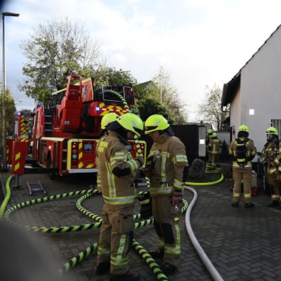 Auf dem Foto sind mehrere Feuerwehrleute vor dem Brandhaus zu sehen. Das Feuer ist bereits gelöscht.