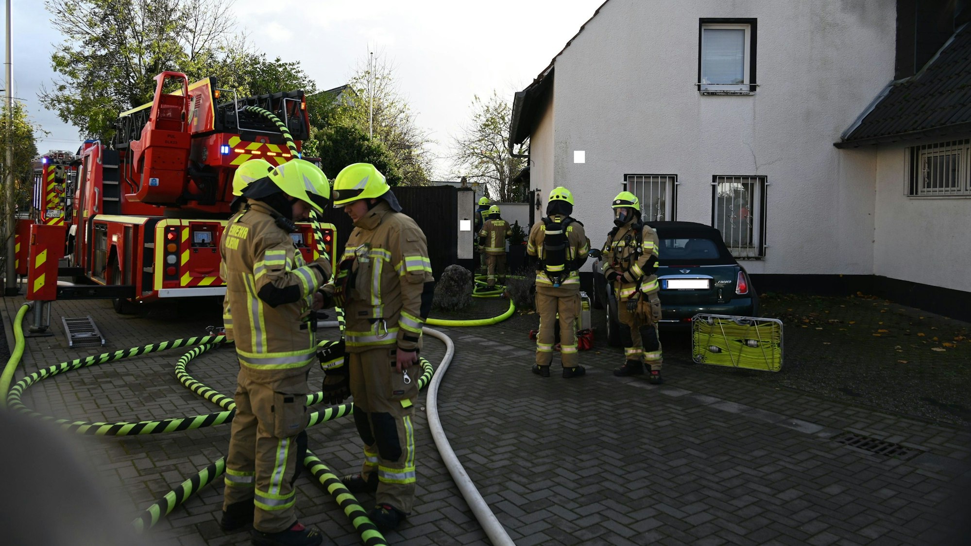 Auf dem Foto sind mehrere Feuerwehrleute vor dem Brandhaus zu sehen. Das Feuer ist bereits gelöscht.