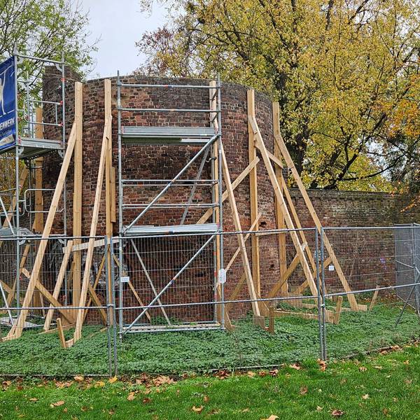 Kanthölzer, Gerüste und ein Bauzaun sichern einen Turm in einer Mauer.