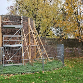 Kanthölzer, Gerüste und ein Bauzaun sichern einen Turm in einer Mauer.