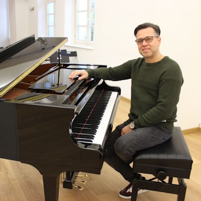 Ein Mann sitzt in einem Saal vor einem Flügel.