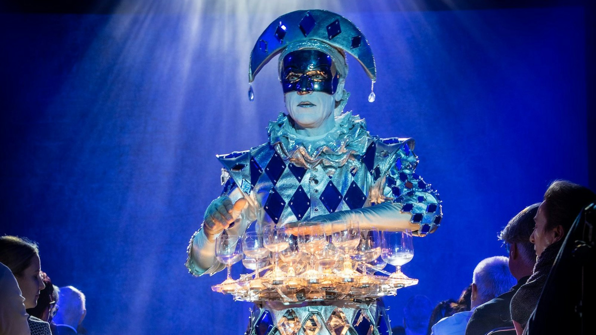 Ein blauer Harlekin spielt auf Gläsern.