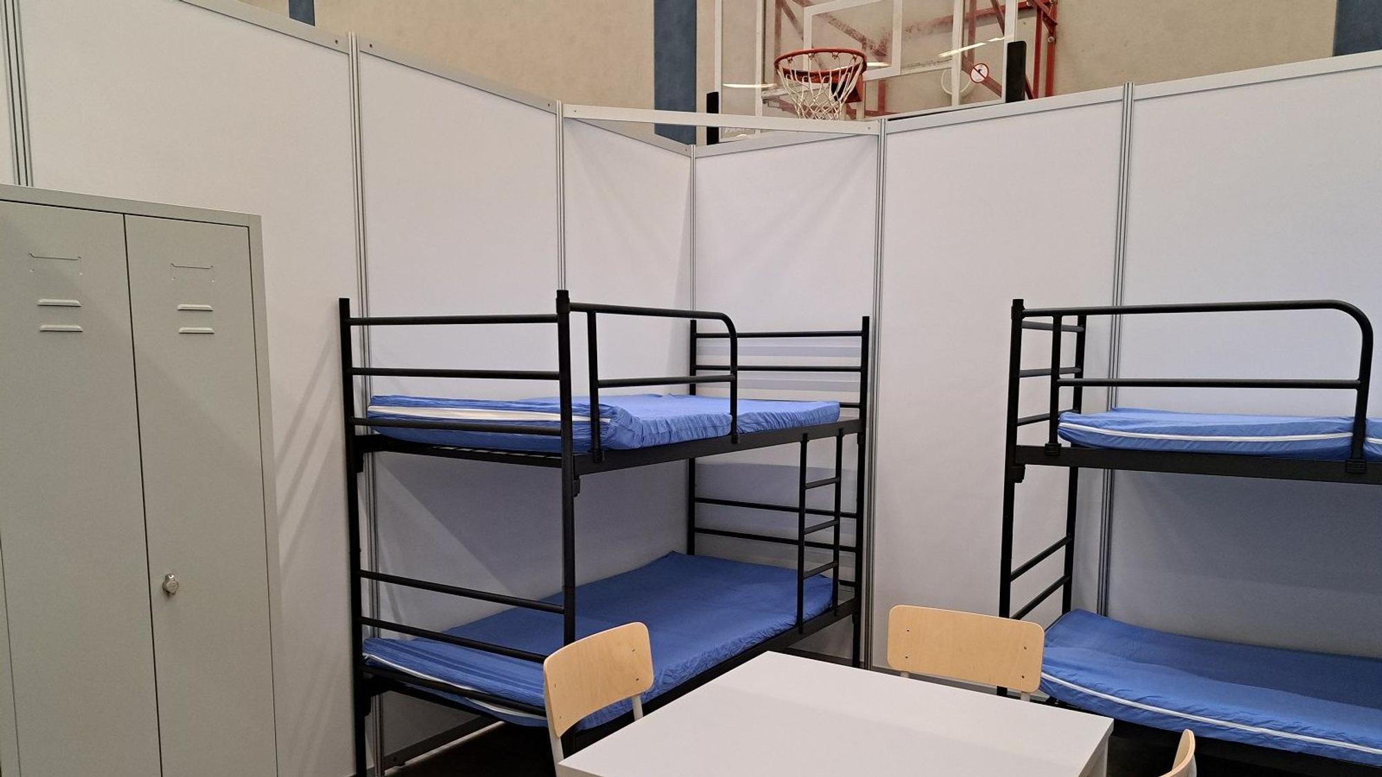 Zu sehen ist eine Wohnbox mit zwei Etagenbetten, einem Tisch mit Stühlen und einem Schrank. Die Wände sind aus Sperrholz, das mit Kunststoff (PVC) beschichtet ist.