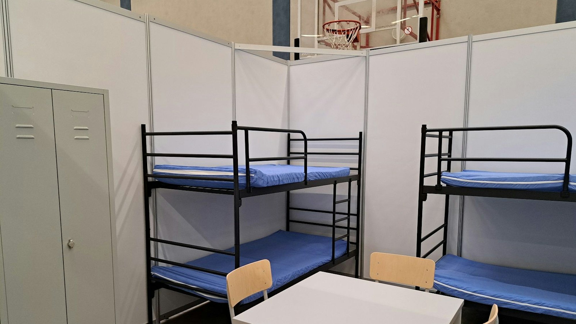 Zu sehen ist eine Wohnbox mit zwei Etagenbetten, einem Tisch mit Stühlen und einem Schrank. Die Wände sind aus Sperrholz, das mit Kunststoff (PVC) beschichtet ist.