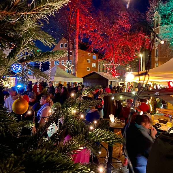 Auf einer Bühne im Freien stehen drei Musiker, vor der Bühne stehen viele Menschen mit Mützen.
