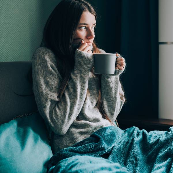 Frau friert auf dem Sofa mit Tasse Tee in der Hand