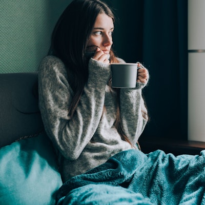 Frau friert auf dem Sofa mit Tasse Tee in der Hand