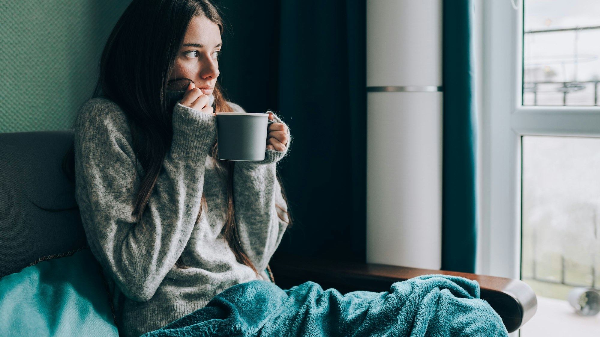 Frau friert auf dem Sofa mit Tasse Tee in der Hand