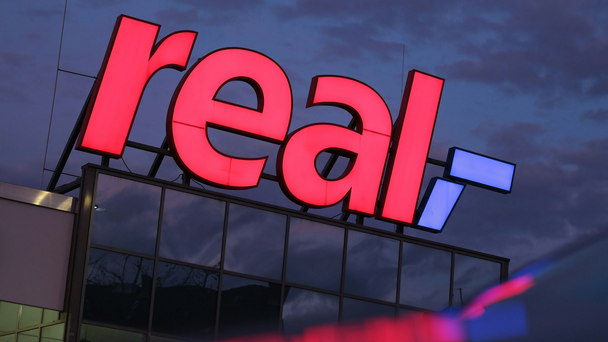 Das Logo leuchtet am Morgen auf dem Dach eines Real Supermarktes.