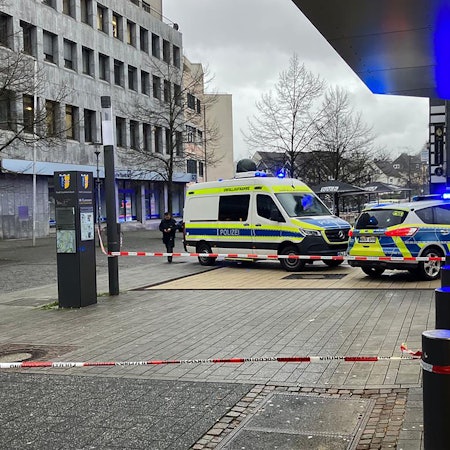 Zwei Polizeiwagen stehen in der Gummersbacher Innenstadt. Um ein Geschäft ist eine Fläche mit Flatterband abgesperrt.