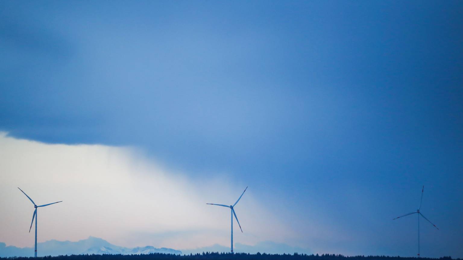 Hinter drei Windrädern ziehen Regenwolken auf.