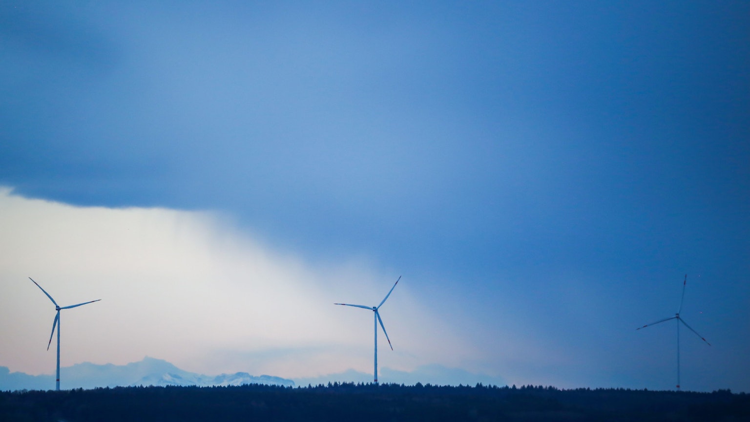 Hinter drei Windrädern ziehen Regenwolken auf.