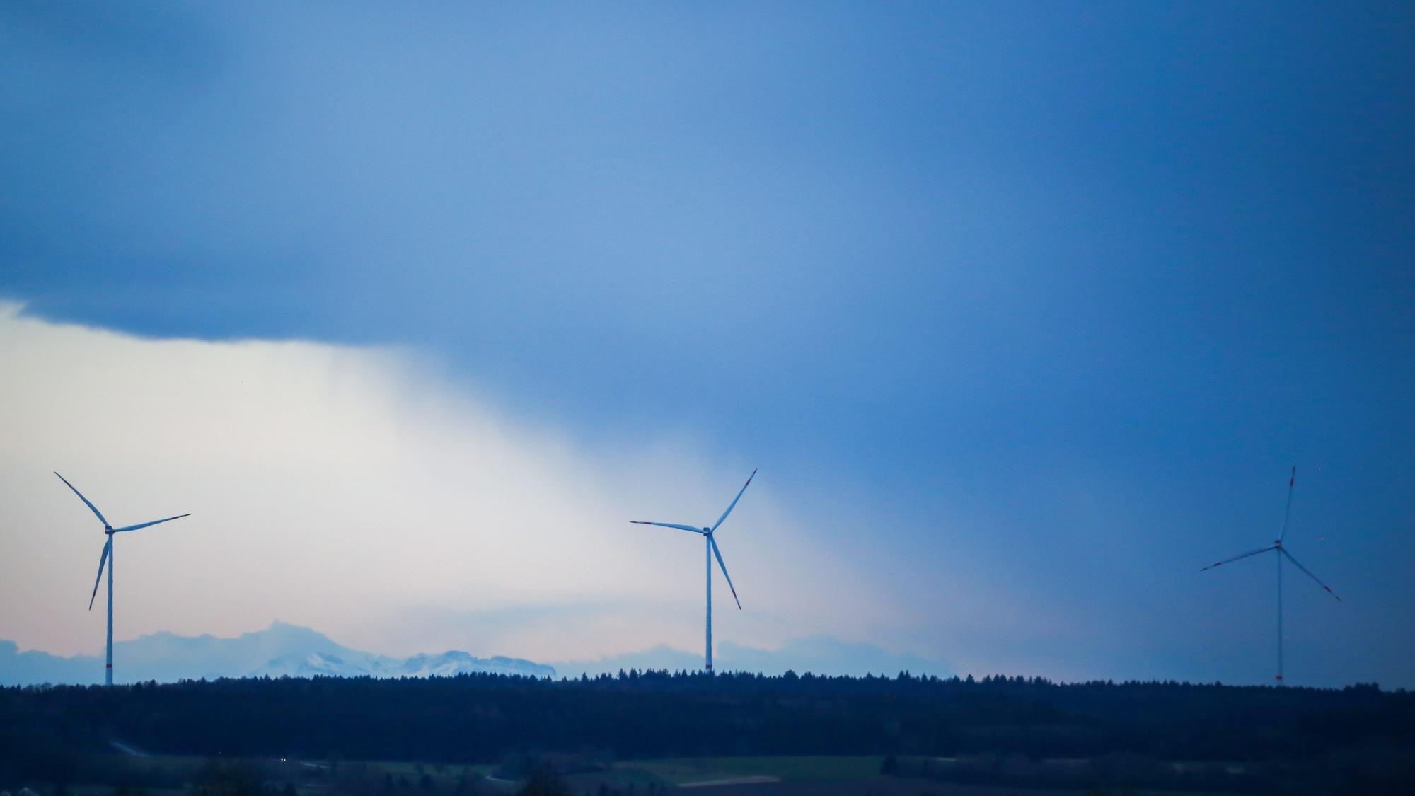 Hinter drei Windrädern ziehen Regenwolken auf.